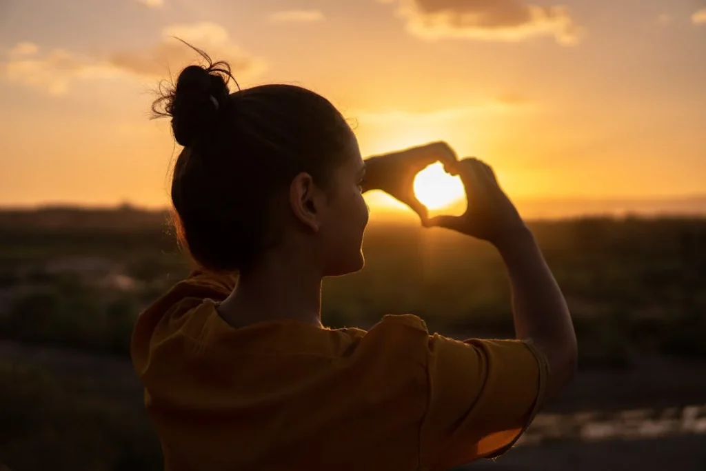 Person making heart shape at sunset