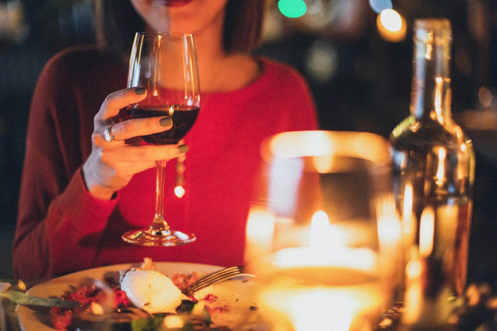 A woman savoring a cozy candlelit dinner with a glass of wine, set in an intimate, warm-toned setting, capturing the elegance and simplicity of enjoying a peaceful dinner.