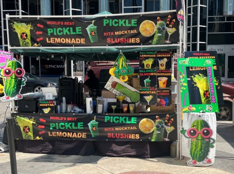 Pickle lemonade stand at street event, colorful signage.